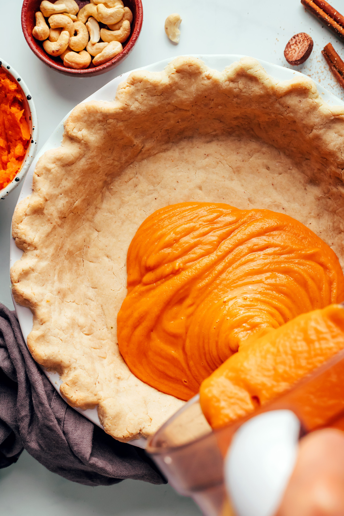 Pouring sweet potato pie filling from a blender into a par-baked pie crust