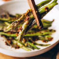 Chopsticks holding spicy stir-fried green beans in front of a bowl